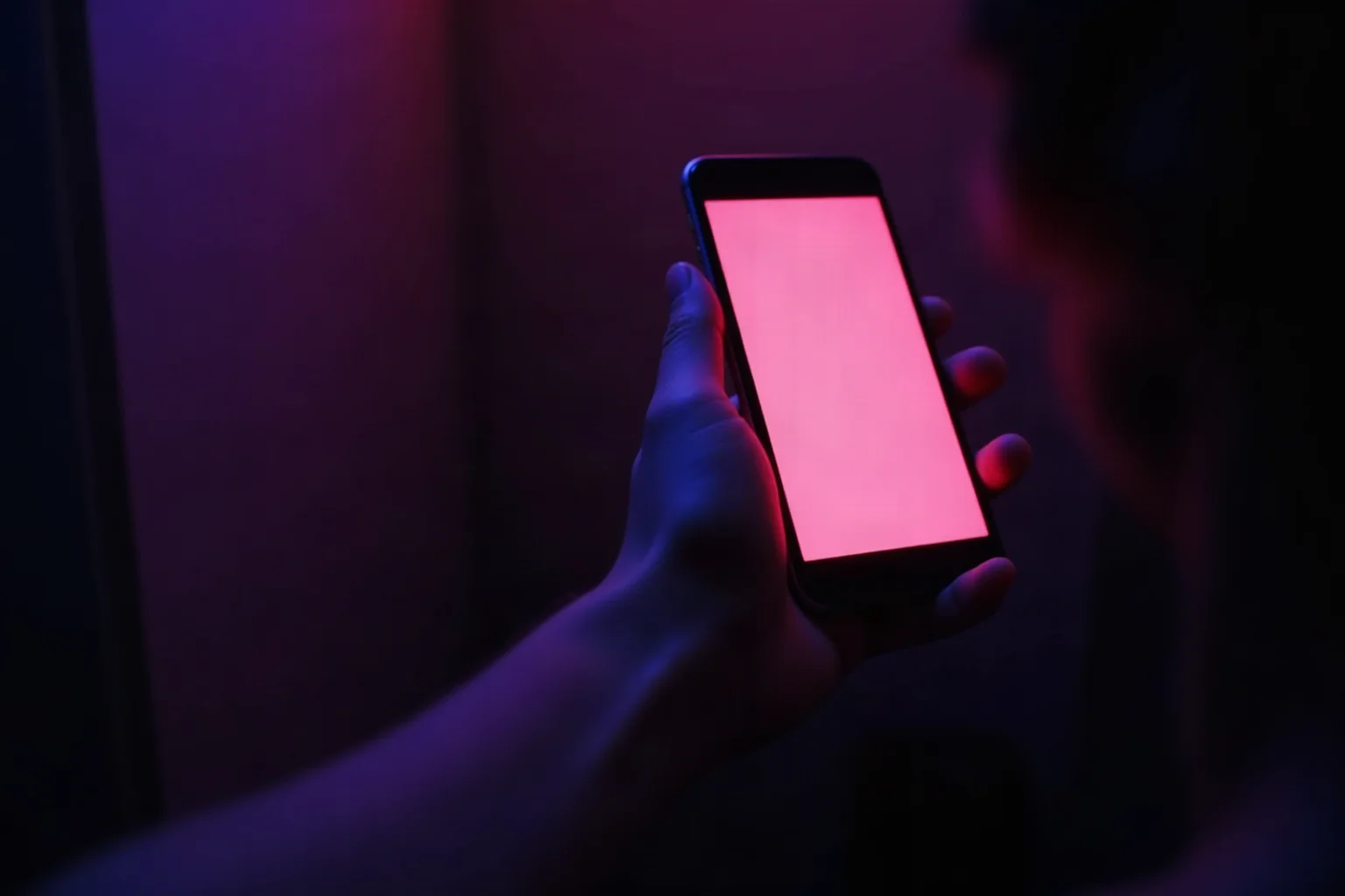 A hand holding a glowing phone in a completely dark room